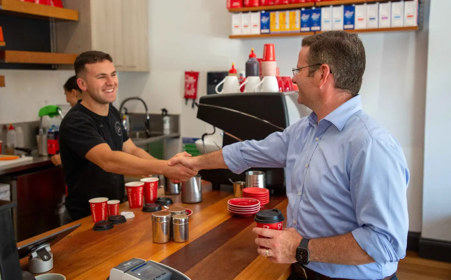 Politician greeting a barista with a handshake at a local cafe