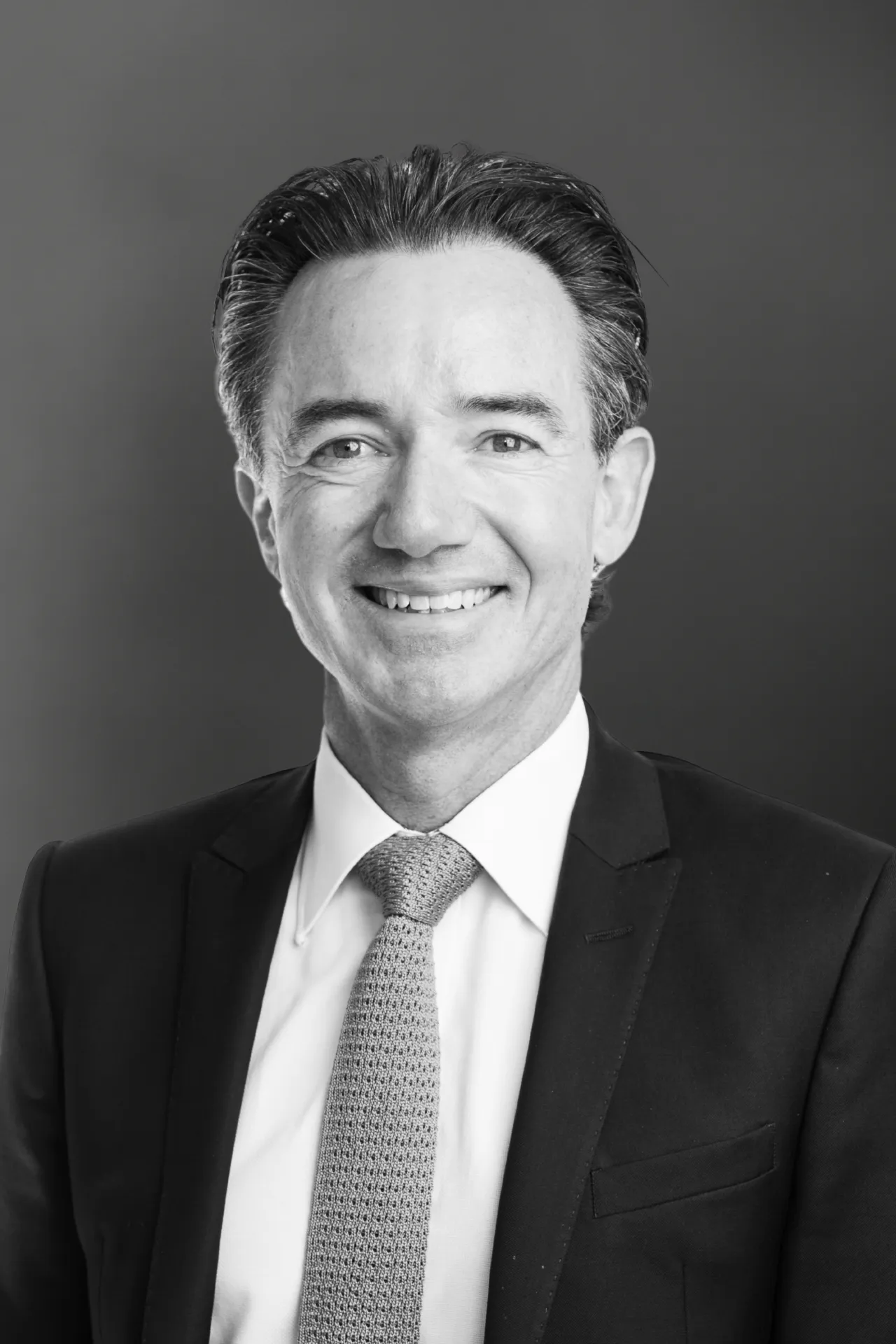 Black and white headshot of a smiling executive in a suit and knitted tie