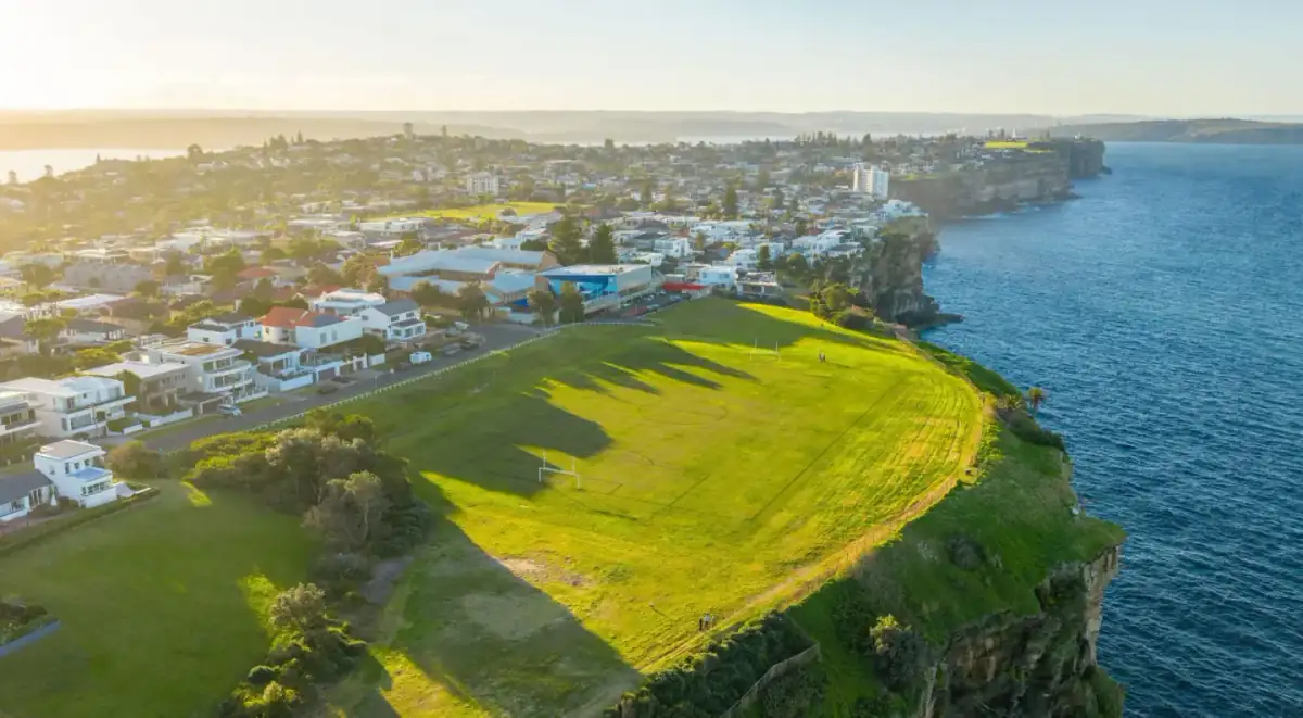 Golden-hour aerial of clifftop homes and parkland above the ocean