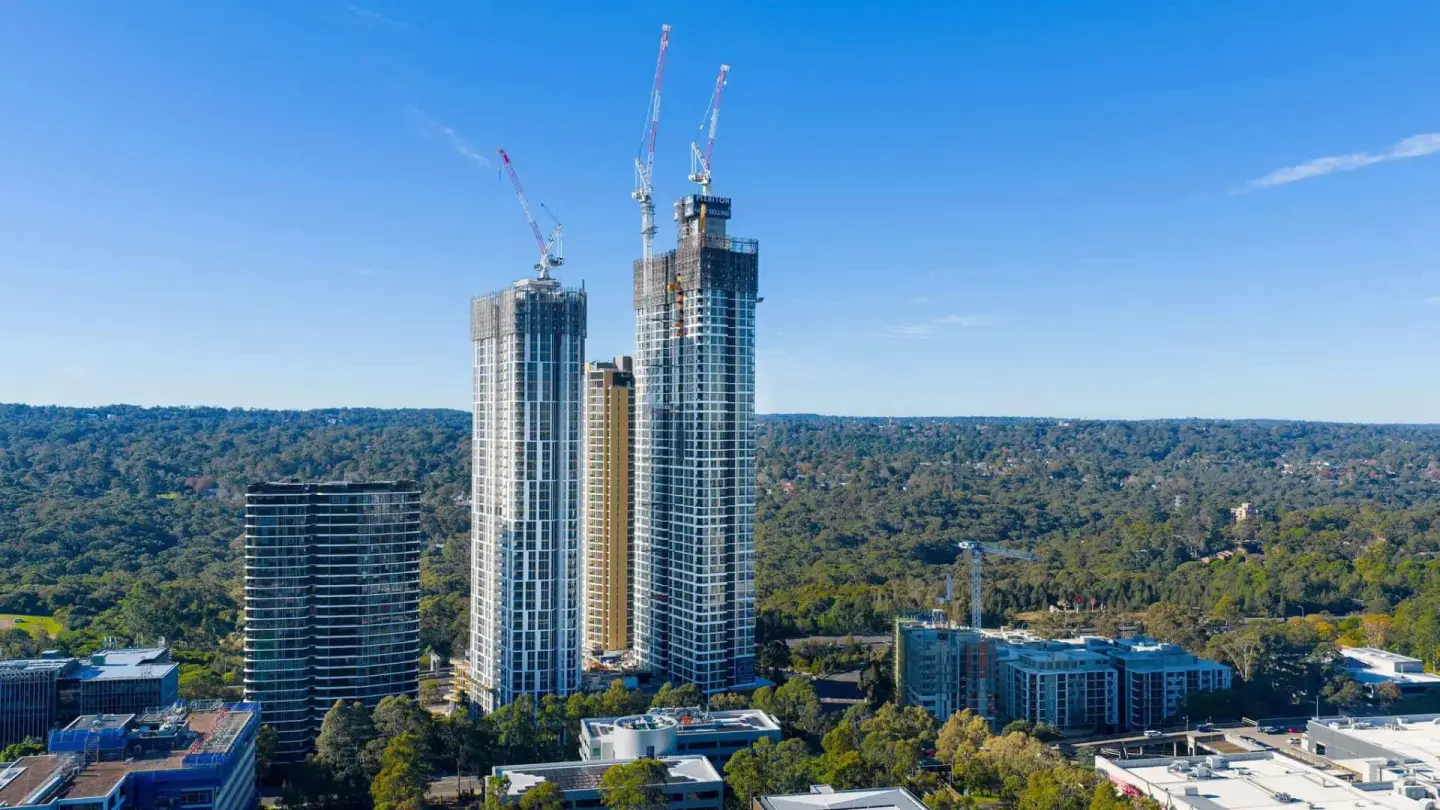 Daytime drone aerial of high-rise construction above the treeline
